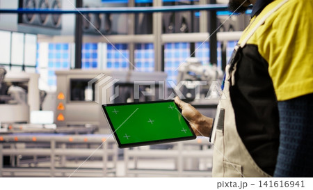 Engineer in smart factory oversees robotic assembly lines using green screen tablet, ensuring quality control. Worker monitoring automated conveyor systems using chroma key device, camera A closeup Engineer in smart factory oversees robotic assembly lines using green screen tablet, ensuring quality control. Worker monitoring automated conveyor systems using chroma key device, camera A closeup 141616941
