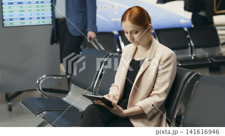 Portrait of modern businesswoman working on laptop in airport departure area, seated near gate with suitcase. Corporate entrepreneur preparing for international business flight. 141616946