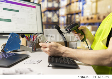 Asian worker scanning and printing shipping labels tags for all orders, using a scanner to register and check stock barcodes for fast delivery operations. Warehouse cargo placed on big racks. 141616969