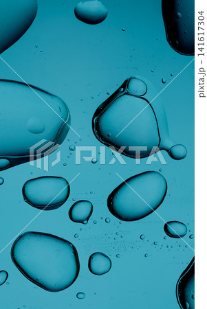 Oil drops floating in water against a teal background, forming abstract organic shapes 141617304