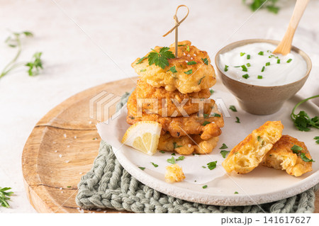 Crispy golden cod fish fritters stacked on a rustic plate with creamy dipping sauce fresh herbs and a lemon wedge for a perfect appetizer snack Crispy golden cod fish fritters stacked on a rustic plate with creamy dipping sauce fresh herbs and a lemon wedge for a perfect appetizer snack 141617627