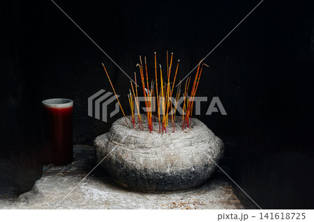 Burning traditional joss incense sticks in a rustic stone burner against dark black background inside chinese temple 141618725