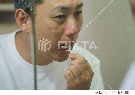 洗面台の鏡の前でデンタルフロスを使う40代男性 洗面台の鏡の前でデンタルフロスを使う40代男性 141620806