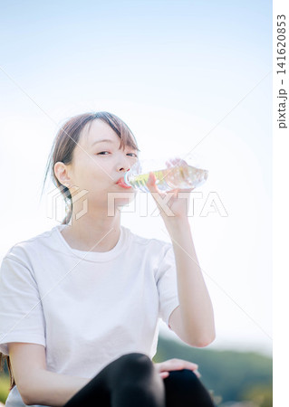 屋外でペットボトルの水を飲み水分補給する女性 屋外でペットボトルの水を飲み水分補給する女性 141620853