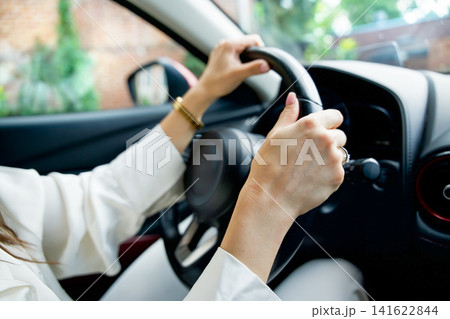 Close up shot of a female driver holding a black steering wheel with both hands, driving a modern car on a city street. Safe driving concept. Close up shot of a female driver holding a black steering wheel with both hands, driving a modern car on a city street. Safe driving concept. 141622844