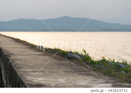Concrete walkway beside calm lake distant mountains warm evening light creating peaceful landscape ideal for travel nature relaxation outdoor backgrounds 141623731