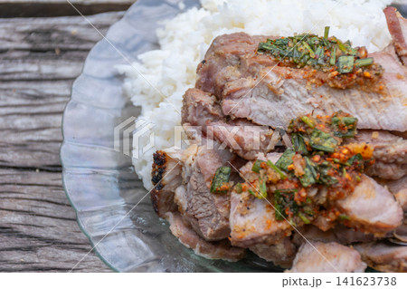 Close up of grilled pork neck served steamed white rice spicy herb chili sauce Traditional Asian comfort food Fresh homemade meal rustic wooden background Close up of grilled pork neck served steamed white rice spicy herb chili sauce Traditional Asian comfort food Fresh homemade meal rustic wooden background 141623738