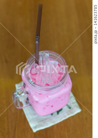 Refreshing pink iced milk drink served glass mug ice cubes straw wooden table perfect for cafe menu dessert beverage summer refreshment 141623785