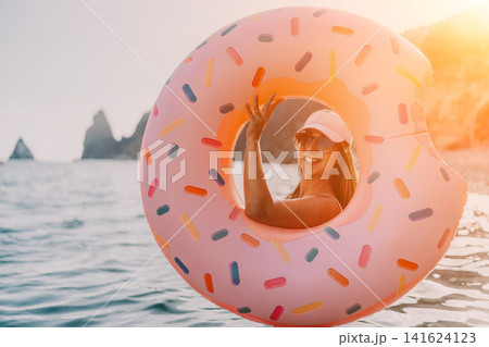 Woman, donut, ocean. Happy woman smiles inside large inflatable donut float with copy space, enjoying summer vacation. 141624123