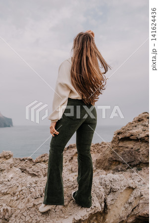Woman cliff ocean young woman with long hair standing on a rocky cliff overlooking the sea under a cloudy sky Woman cliff ocean young woman with long hair standing on a rocky cliff overlooking the sea under a cloudy sky 141624436