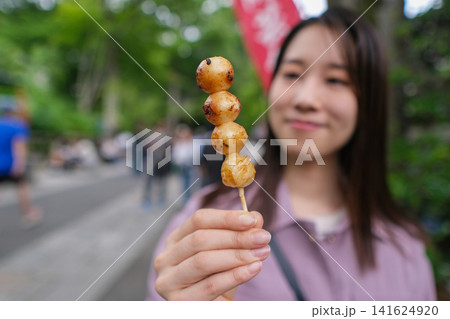 東京のレトロな観光地(深大寺近くの公道)で食べ歩きする女性が持つお団子のクローズアップ 東京のレトロな観光地(深大寺近くの公道)で食べ歩きする女性が持つお団子のクローズアップ 141624920