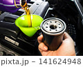 Pouring fresh motor oil through a green funnel into the car engine with a new oil filter 141624948