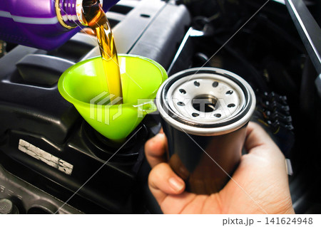 Pouring fresh motor oil through a green funnel into the car engine with a new oil filter Pouring fresh motor oil through a green funnel into the car engine with a new oil filter 141624948