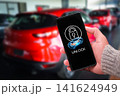 Hand holding a smartphone using a smart digital key application to unlock a modern red car remotely 141624949