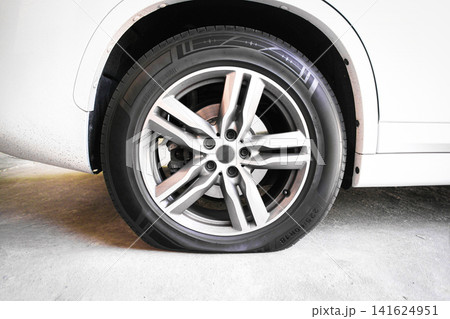 Close-up of a flat tire on a white modern car parked on a concrete floor Close-up of a flat tire on a white modern car parked on a concrete floor 141624951