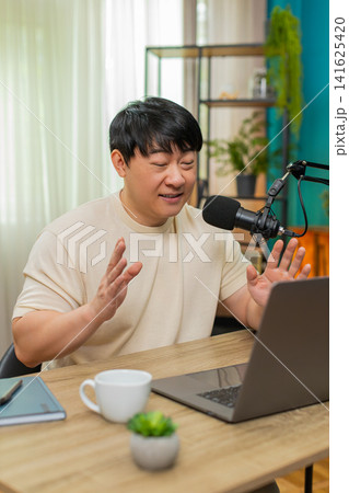 Asian man hosting live stream with studio mic and headphones, engaging speaking to audience online 141625420
