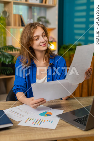 Young woman on home table checking documents finds needed point and nods with satisfied happy smile Young woman on home table checking documents finds needed point and nods with satisfied happy smile 141625561