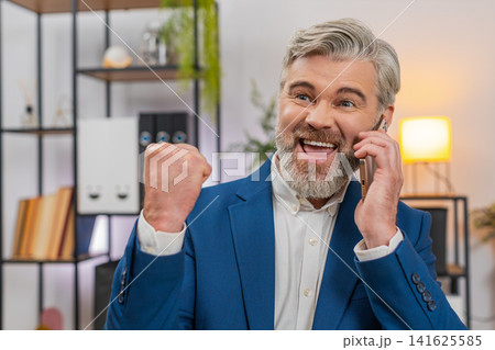 Middle-aged businessman cheers with smartphone celebrates promotion after hearing great news on call Middle-aged businessman cheers with smartphone celebrates promotion after hearing great news on call 141625585