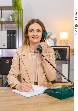 Businesswoman calls client on retro phone spins rotary dial takes notes agreement formal tone smile Businesswoman calls client on retro phone spins rotary dial takes notes agreement formal tone smile 141625592