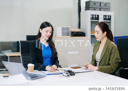 Asian businesswoman signs a car loan contract, receives the vehicle key, and shakes hands with a finance agent. Ideal for commercial auto insurance 141625884