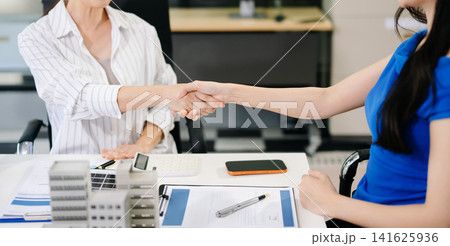 Asian female professionals shaking hands over a miniature building model during a real estate project or property investment agreement. 141625936