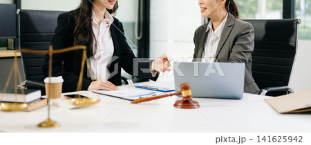 Two professional Asian female attorneys discussing legal documents and using a laptop in a modern law office workspace. Two professional Asian female attorneys discussing legal documents and using a laptop in a modern law office workspace. 141625942
