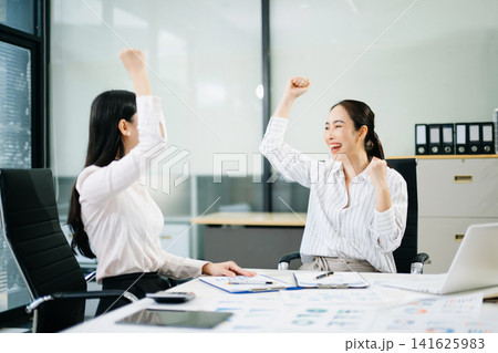 Two cheerful professional female colleagues raise their fists in celebration of a business achievement, major deal, or financial Two cheerful professional female colleagues raise their fists in celebration of a business achievement, major deal, or financial 141625983