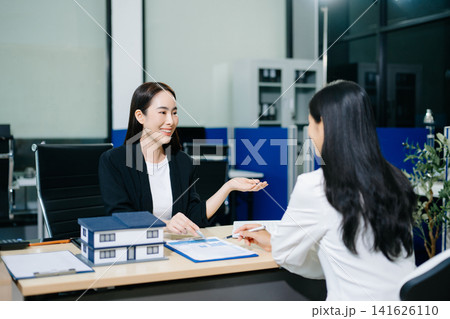 Professional Asian real estate consultant presenting a house model to a client during a property investment meeting in a modern office. Professional Asian real estate consultant presenting a house model to a client during a property investment meeting in a modern office. 141626110