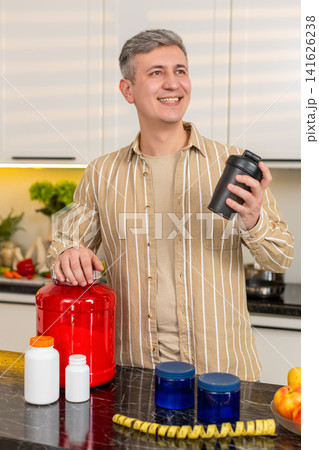 Middle-aged man enjoying protein shake in kitchen at home after mixing protein powder for meal plan Middle-aged man enjoying protein shake in kitchen at home after mixing protein powder for meal plan 141626238