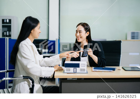 Real estate broker agent presenting and consult to customer to decision making sign insurance form agreement, home model, concerning mortgage loan offer in office Real estate broker agent presenting and consult to customer to decision making sign insurance form agreement, home model, concerning mortgage loan offer in office 141626325
