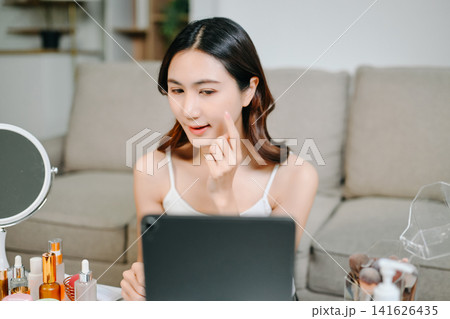 Asian beauty influencer filming a makeup tutorial using cosmetics, skincare products, smartphone and ring light in a modern home studio for social media content. Asian beauty influencer filming a makeup tutorial using cosmetics, skincare products, smartphone and ring light in a modern home studio for social media content. 141626435