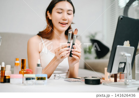 Asian beauty influencer filming a makeup tutorial using cosmetics, skincare products, smartphone and ring light in a modern home studio for social media content. Asian beauty influencer filming a makeup tutorial using cosmetics, skincare products, smartphone and ring light in a modern home studio for social media content. 141626436
