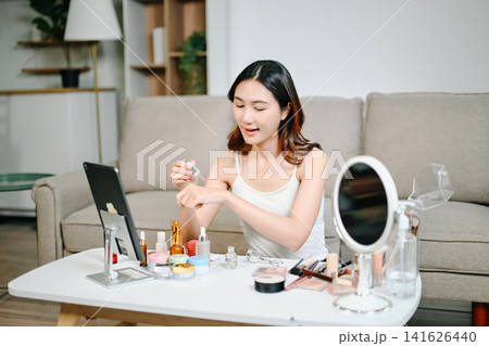 Asian beauty influencer filming a makeup tutorial using cosmetics, skincare products, smartphone and ring light in a modern home studio for social media content. Asian beauty influencer filming a makeup tutorial using cosmetics, skincare products, smartphone and ring light in a modern home studio for social media content. 141626440