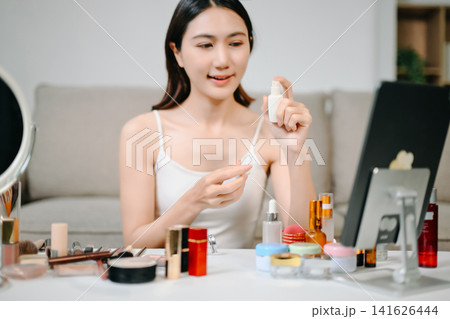 Asian beauty influencer filming a makeup tutorial using cosmetics, skincare products, smartphone and ring light in a modern home studio for social media content. Asian beauty influencer filming a makeup tutorial using cosmetics, skincare products, smartphone and ring light in a modern home studio for social media content. 141626444