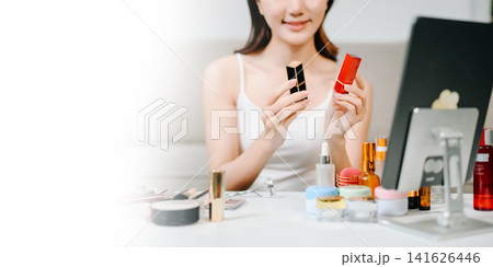 Asian woman carefully applies lipstick in front of a vanity mirror, highlighting her daily beauty and makeup routine. Asian woman carefully applies lipstick in front of a vanity mirror, highlighting her daily beauty and makeup routine. 141626446