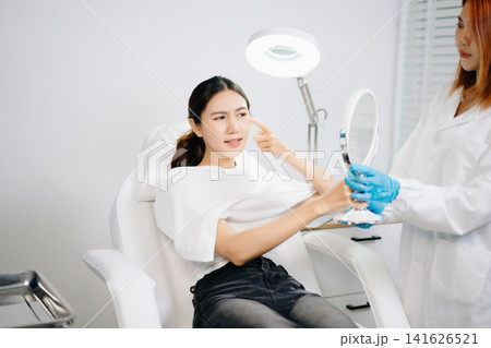 Doctor consulting patient in beauty clinic with facial analysis and skincare planning. Professional aesthetic treatment, clean sterile care, modern dermatology for radiant skin. Doctor consulting patient in beauty clinic with facial analysis and skincare planning. Professional aesthetic treatment, clean sterile care, modern dermatology for radiant skin. 141626521