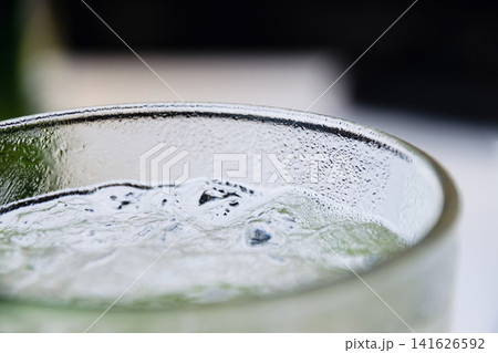 Close up of condensation on a clear glass filled with refreshing ice cold liquid beverage Close up of condensation on a clear glass filled with refreshing ice cold liquid beverage 141626592