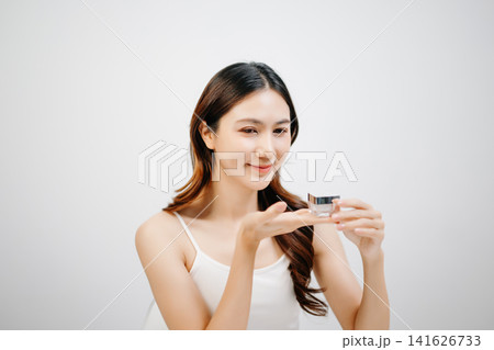 Asian woman presenting skincare product with clean minimal aesthetic, glowing skin and beauty routine concept for cosmetic advertising 141626733