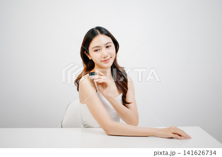 Asian woman presenting skincare product with clean minimal aesthetic, glowing skin and beauty routine concept for cosmetic advertising Asian woman presenting skincare product with clean minimal aesthetic, glowing skin and beauty routine concept for cosmetic advertising 141626734