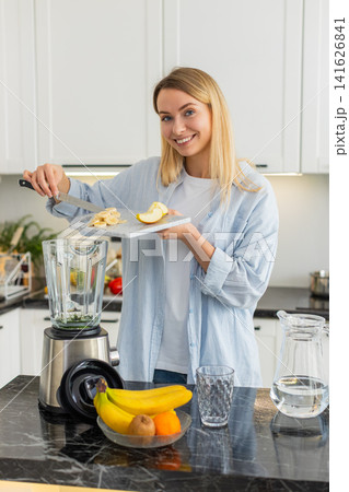 Young woman making smoothie adding banana apple spinach spirulina to blender detox in home kitchen Young woman making smoothie adding banana apple spinach spirulina to blender detox in home kitchen 141626841