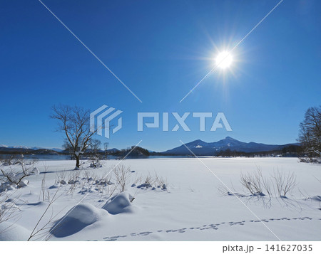 冬の裏磐梯、桧原湖。半凍結した白い輝き雪原と遠方の磐梯山、快晴の青空に太陽が輝き、印象的で綺麗だ。 141627035
