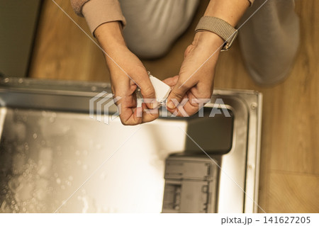 Woman unwrapping dishwasher detergent tablet before loading kitchen appliance 141627205