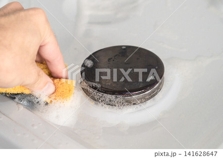 Photo of manual cleaning of the surface of a gas stove from small dirt with a cleaning agent and a greenhouse household sponge Photo of manual cleaning of the surface of a gas stove from small dirt with a cleaning agent and a greenhouse household sponge 141628647