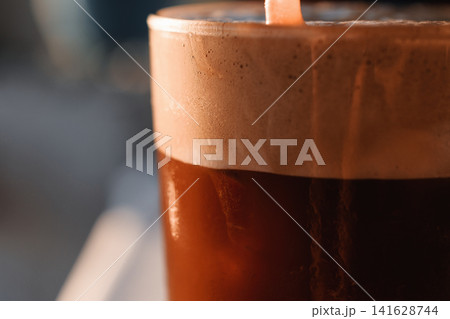 Refreshing cold coffee drink with abundant foam topping and ice cubes in a clear glass with straw Refreshing cold coffee drink with abundant foam topping and ice cubes in a clear glass with straw 141628744