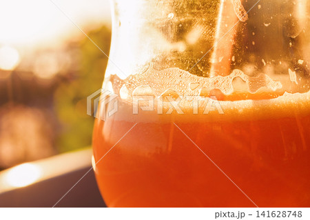 Close up of vibrant orange juice with foam and bubbles in a glass on a sunny day in a garden Close up of vibrant orange juice with foam and bubbles in a glass on a sunny day in a garden 141628748