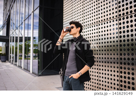 Man drinking coffee on city street by modern building Man drinking coffee on city street by modern building 141629149