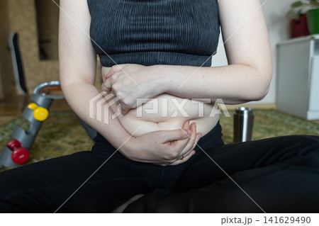 Woman demonstrating belly fat before doing yoga for weight loss and breathing exercises. Concept of body positivity, self love, and home fitness. Woman demonstrating belly fat before doing yoga for weight loss and breathing exercises. Concept of body positivity, self love, and home fitness. 141629490