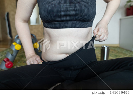 Woman demonstrating belly fat before doing yoga for weight loss and breathing exercises. Concept of body positivity, self love, and home fitness. 141629493