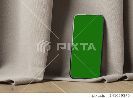 Blank smartphone mockup leaning against fabric on a wooden floor. Green screen mobile phone in an indoor interior. App design and advertising template.. 141629570