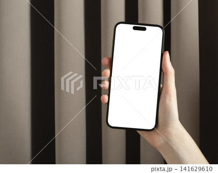 Hand holding smartphone with blank screen. Vertical mobile phone mockup against striped curtain background. Copy space for app advertising and UI design.. Hand holding smartphone with blank screen. Vertical mobile phone mockup against striped curtain background. Copy space for app advertising and UI design.. 141629610